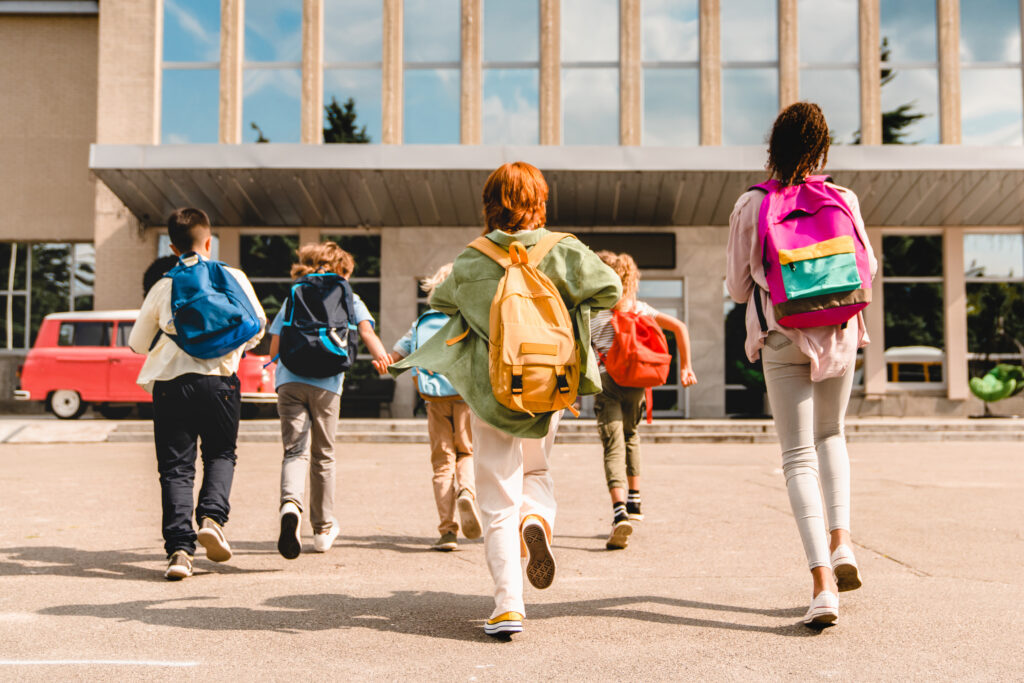 Group of diverse primary school pupils walking together into school with backpacks